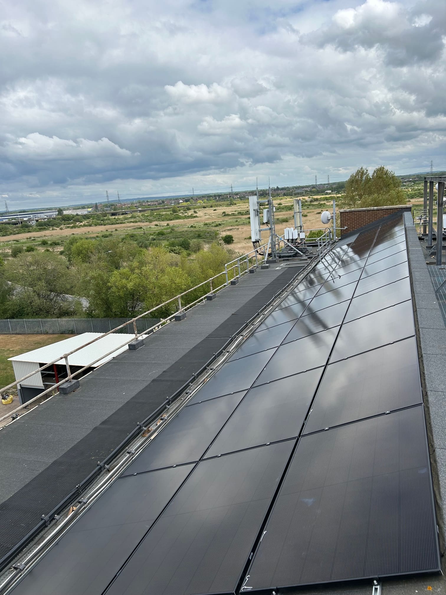Long run of the solar array along the flat-roof edge of the Rainham workshop with open landscape beyond