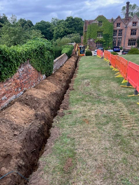 Long cable trench dug along the historic walled garden at Seckford Hall with a mini digger