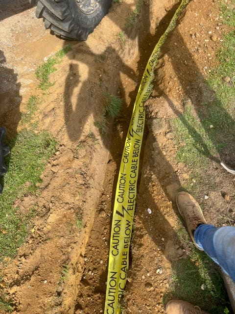 Yellow electric cable warning tape being laid over cables in a trench at Seckford Hall